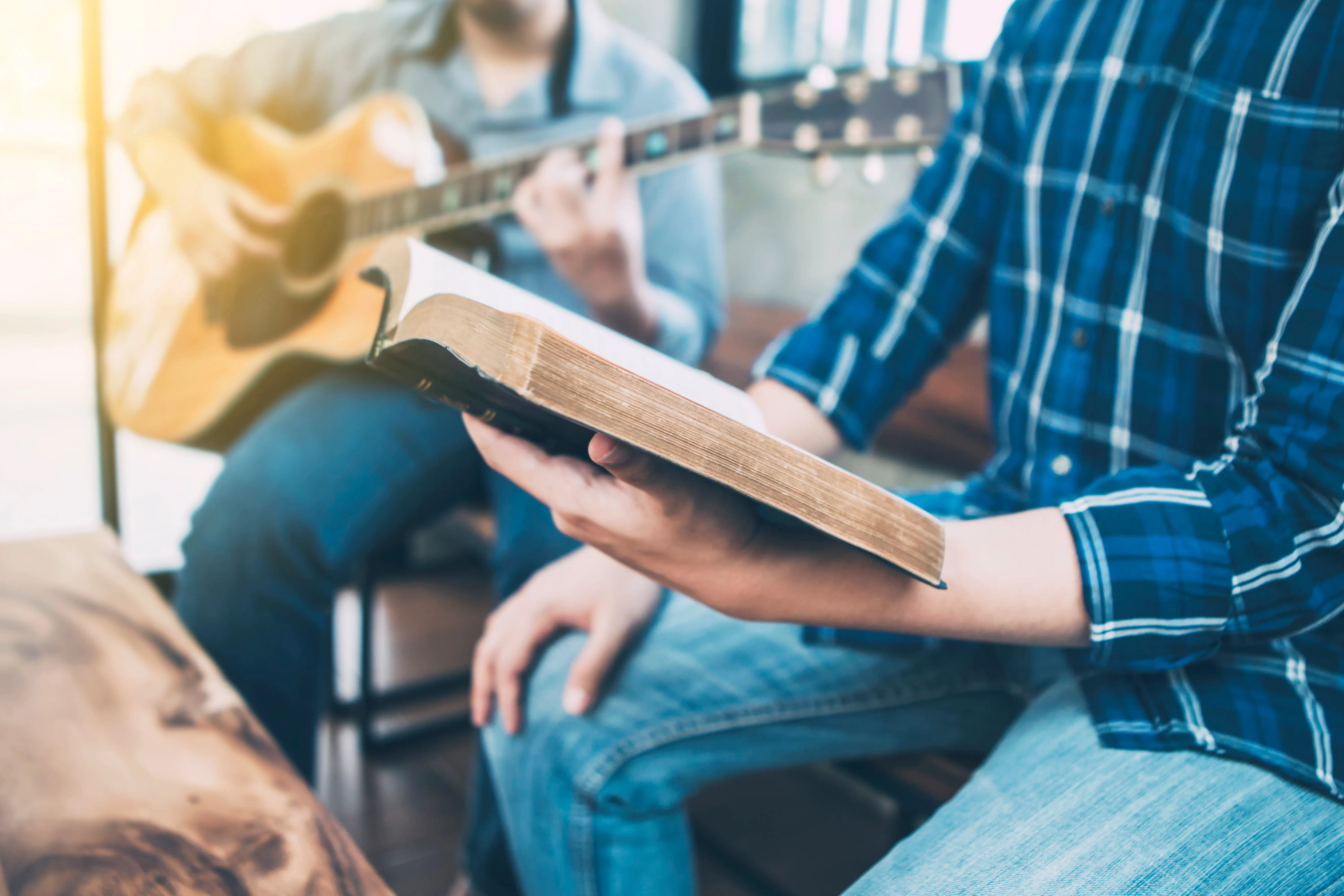 man reading Bible sitting next to man playing guitar